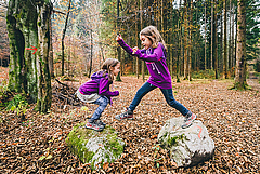 Eineiige Zwillinge springen beim Wandern in Slowenien von Felsen in einem Wald. (Bild: _jure / Adobe Photo Stock)