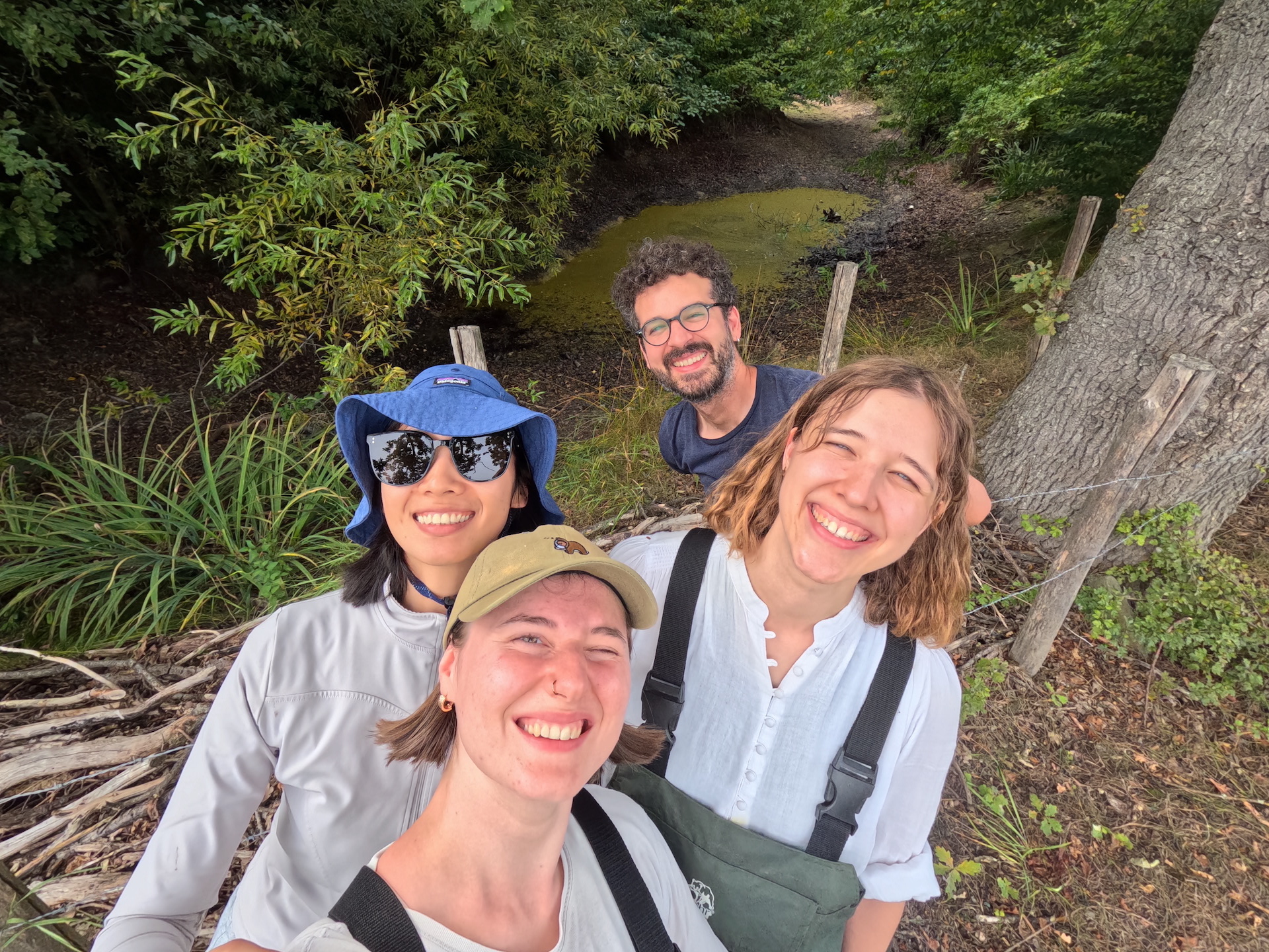 idiv-Team of four young scientist take a selfie in front of a nearly dried up pond amidst trees and other vegetation.