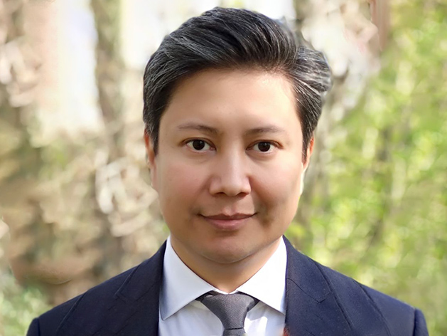 idiv-Man with short dark hair wearing a suit jacket, white shirt, and tie, looking straight at the camera with a neutral expression