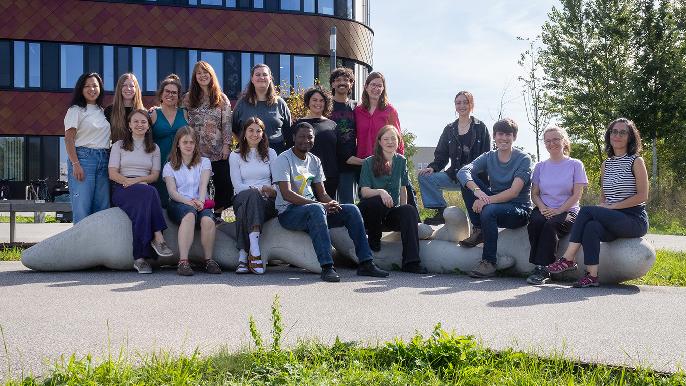 idiv-Group of people sitting and standing outdoors on a curved concrete bench in front of a modern building and trees